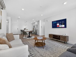 Ein modernes Wohnzimmer mit einem weißen Sofa, einem Couchtisch und einem flachbildfernseher an der Wand, der verschiedene Streaming-Dienste anzeigt.