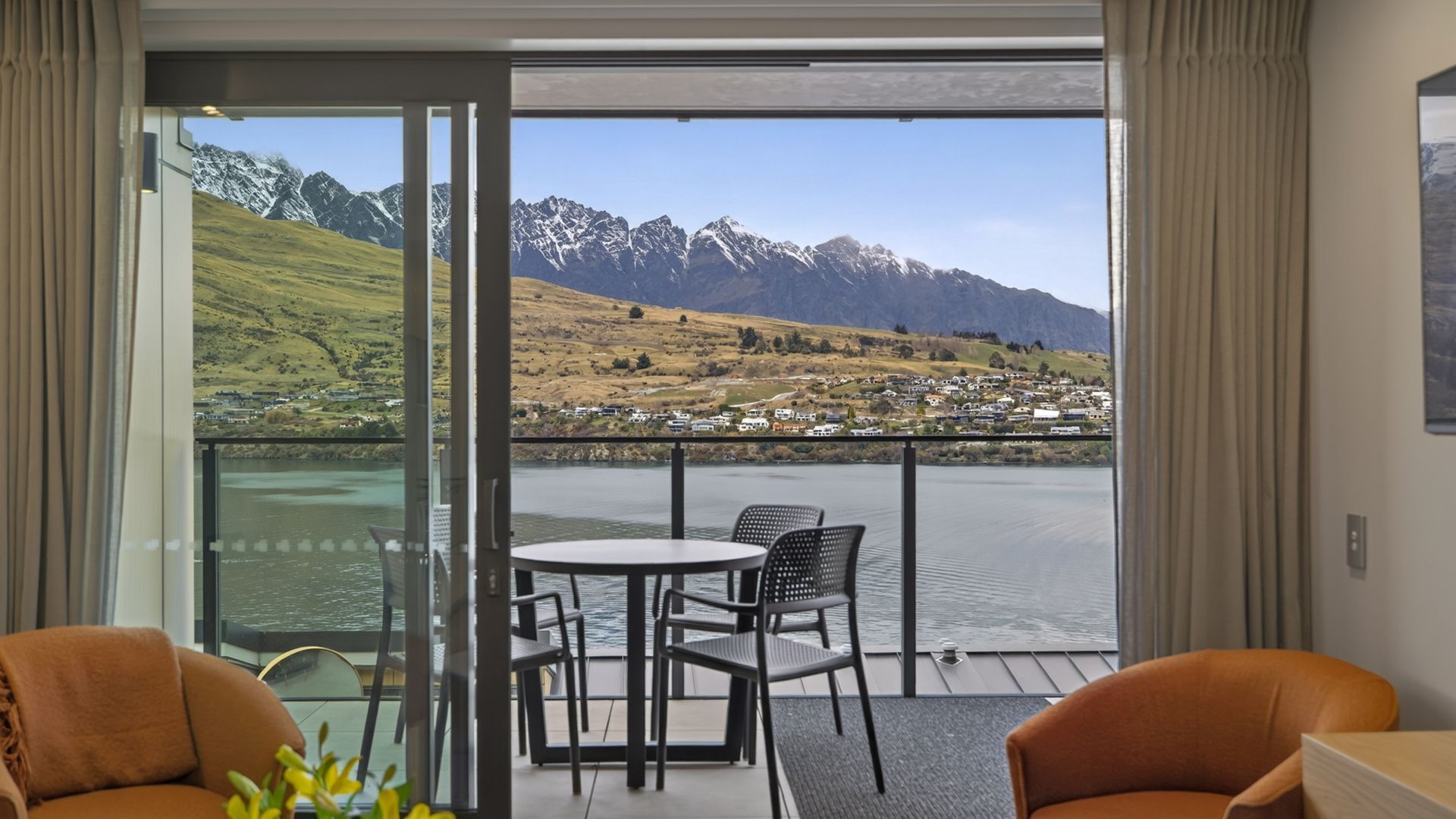 Een kamer met balkon, met uitzicht op een meer en bergen. Op het balkon staan een tafel en twee stoelen.