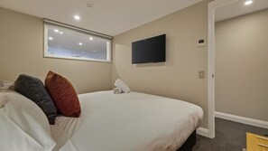 Ein Schlafzimmer mit Bett, Kissen, einem Flachbildfernseher, einem Fenster und einer Tür.