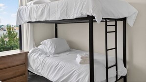 Un lit superposé avec une literie blanche et une commode en bois.