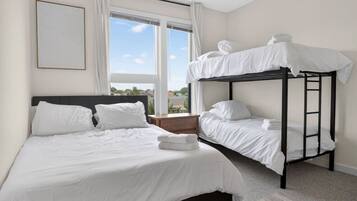 A hotel room with a bunk bed, a single bed, and a large window offering a view.