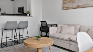 A modern living room with a sofa, two bar stools, a round wooden coffee table, and a television. - NEW! LUX 1BR w/ 400 Mbps Wifi | ROKU TV & Games! (Chelsea)