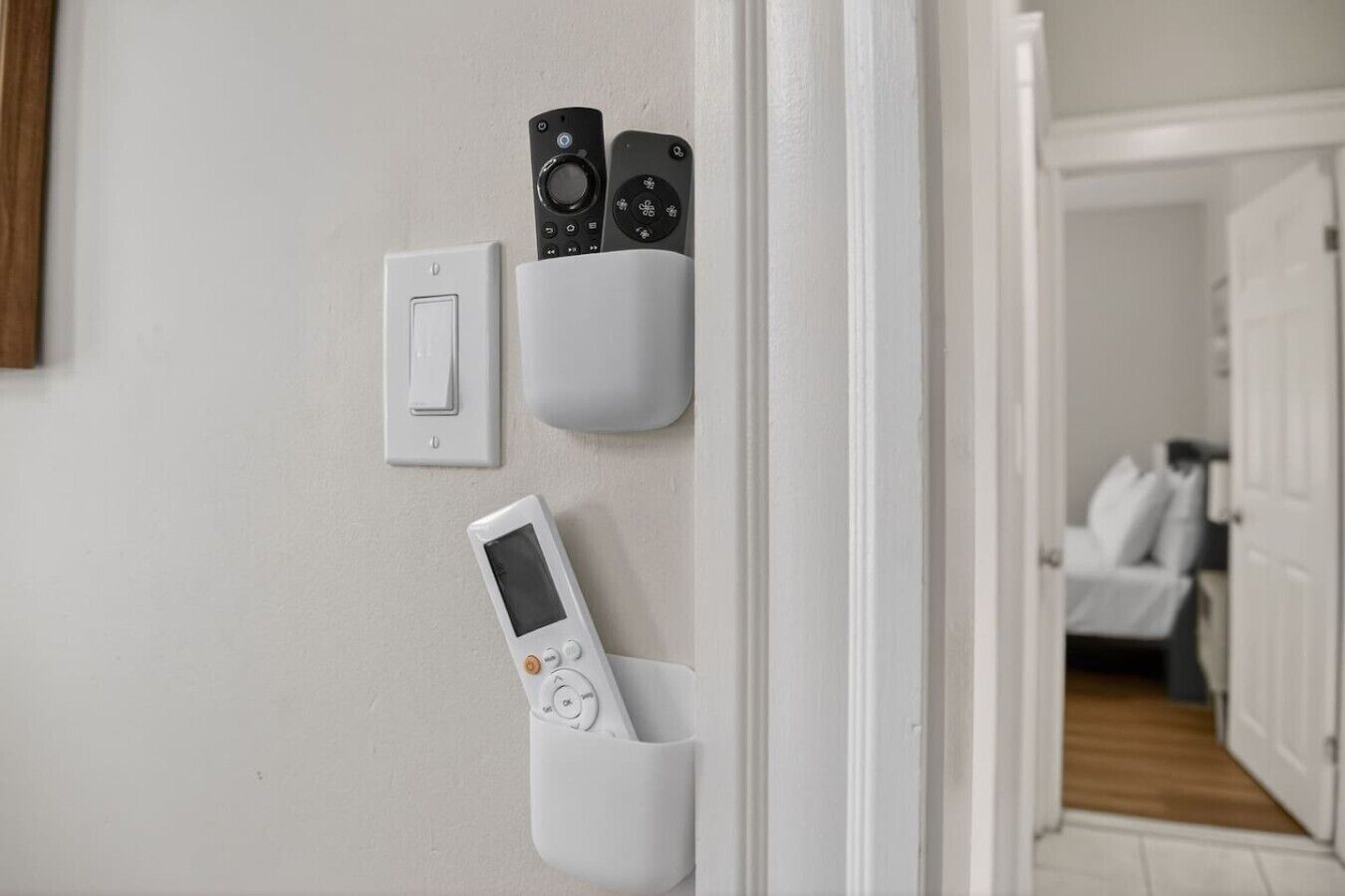 A wall-mounted control panel with a light switch and two remote controls in a hallway.
