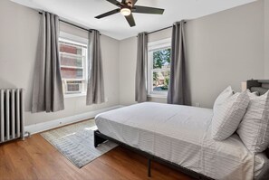 A bedroom with a bed, a ceiling fan, a radiator, and a view of the outside. - 3BR Boston Stay | 2 Balconies + Views (Boston)