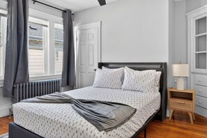 A bedroom with a bed, a nightstand, a lamp, and a window with curtains.