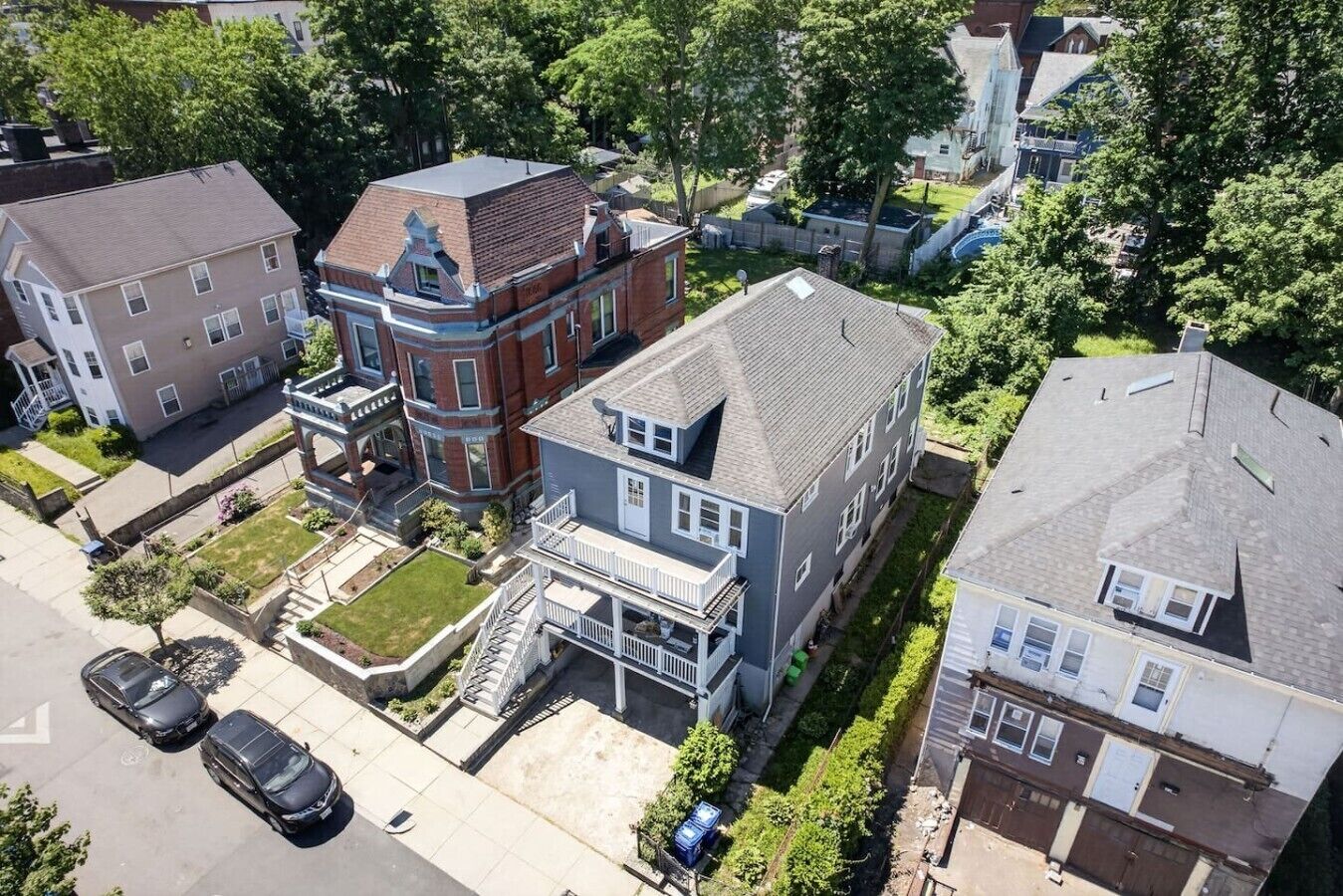 A multi-story residential building with a prominent corner entrance, a front porch, and a small front yard.