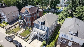 A multi-story residential building with a prominent corner entrance, a front porch, and a small front yard.