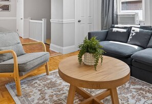 A living room with a round wooden coffee table, a grey sofa, a wooden armchair, and a patterned rug.