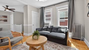 A modern living room with a grey sofa, a round wooden coffee table, and a ceiling fan.