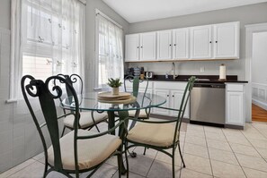 A modern kitchen with white cabinets, a stainless steel dishwasher, and a glass dining table with chairs. - 3BR Boston Stay | 2 Balconies + Views (Boston)