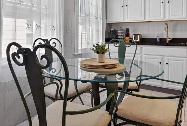 A modern kitchen with white cabinets, a glass table, and metal chairs.