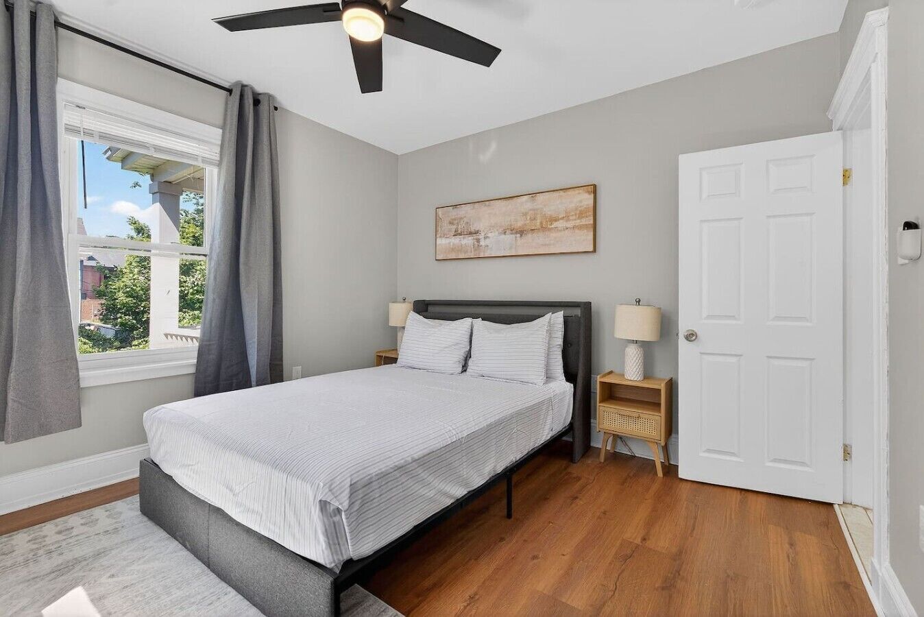 Une chambre à coucher avec un lit, un ventilateur de plafond, une table de chevet, une lampe et une porte.