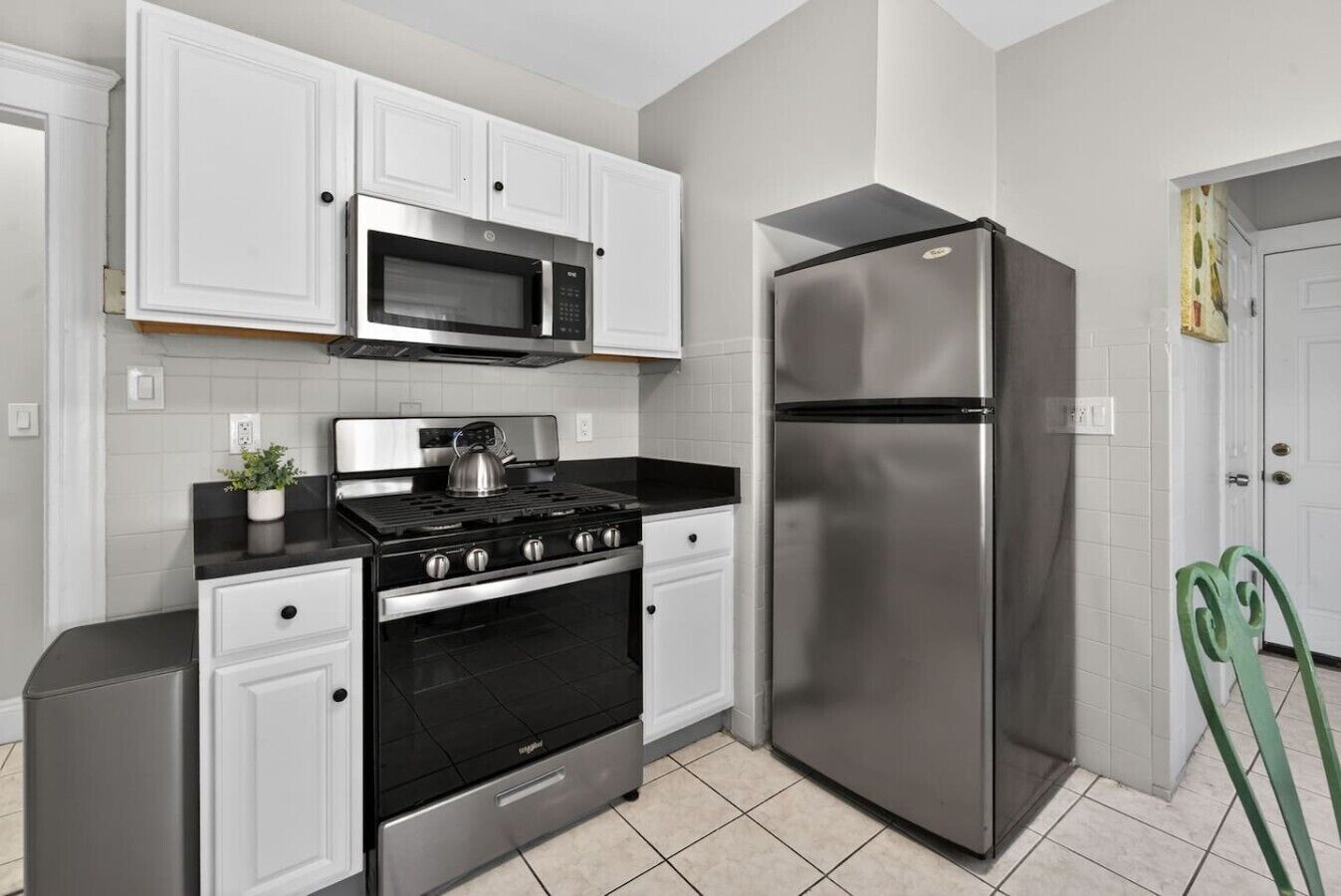 A kitchen with white cabinets, a stainless steel stove, a microwave, and a refrigerator.