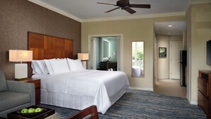 Ein Hotelzimmer mit Bett, Schreibtisch, Sessel, Fernseher und Deckenventilator.