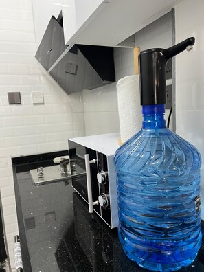 Eine Küche mit schwarzem Arbeitsplatz, einem großen blauen Wasserspender und einer weißen, gefliesten Rückwand.