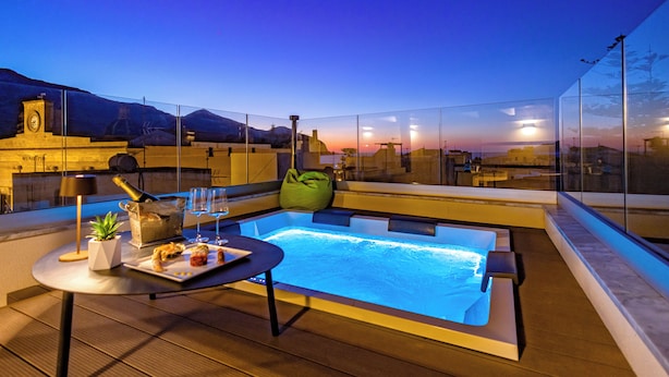 Une terrasse sur le toit avec un jacuzzi, une table avec des boissons et une vue sur le paysage urbain au crépuscule.