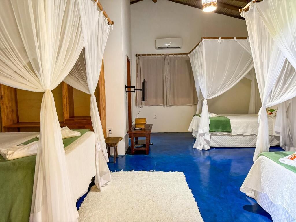 A room with four beds, each with a canopy, a small table, and an air conditioning unit on the wall.