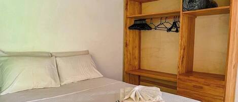 A neatly made bed with a white bedspread and pillows, a wooden wardrobe with a hanging rack, and a single red rose on the bed.