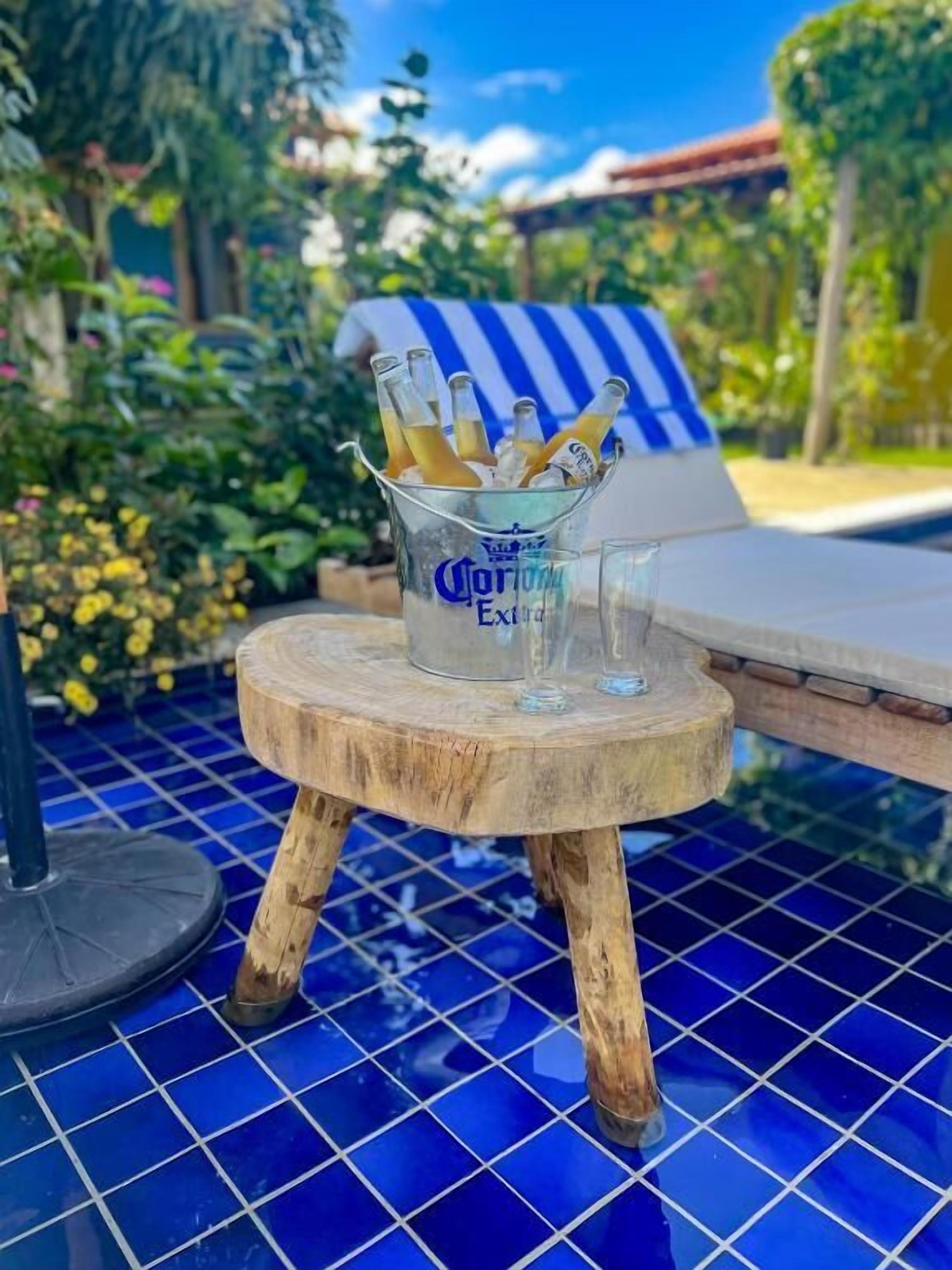 A small wooden stool with a glass containing bottles of Corona Extra, placed on a blue-tiled floor.