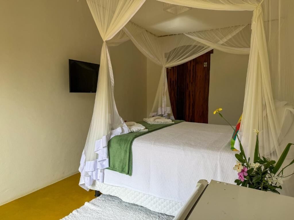 A single bed with a canopy, a flat-screen TV mounted on the wall, and a bedside table with a vase of flowers.