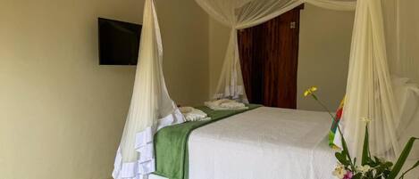 A single bed with a canopy, a flat-screen TV mounted on the wall, and a bedside table with a vase of flowers.