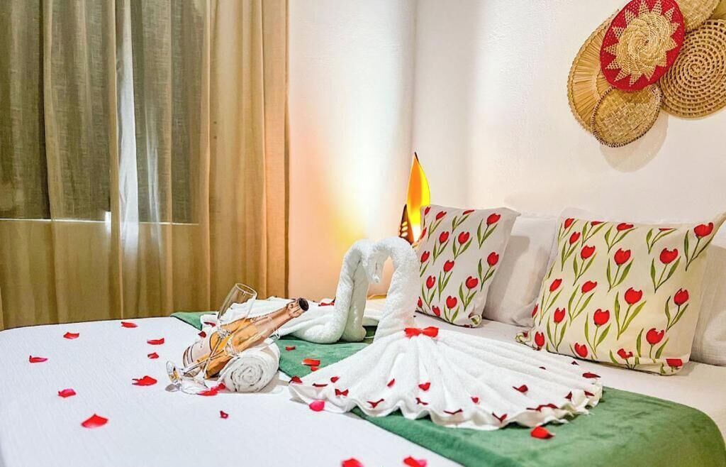 A hotel room with a bed, pillows, a decorative wall hanging, a candle, and a swan-shaped towel.