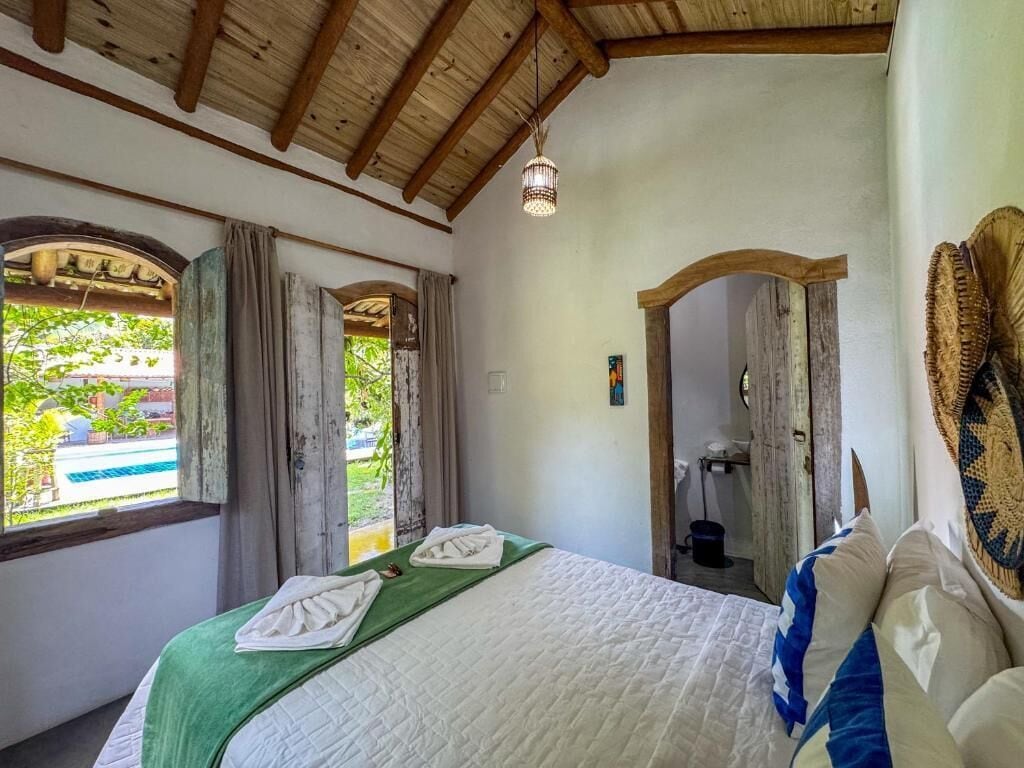 Une pièce avec un lit, une fenêtre avec des rideaux, un plafond en bois et un luminaire suspendu.