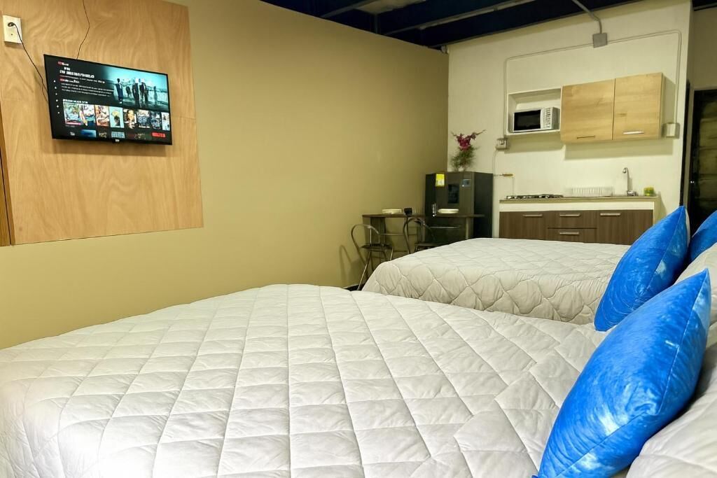 A hotel room with two beds, a television mounted on the wall, a kitchenette, and a microwave above the cabinets.