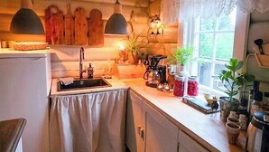 Eine Küche mit Holzbalkendecke, einem Spülbecken, Schränken, einem gemusterten Teppich und einem Fenster mit Spitzenvorhängen.