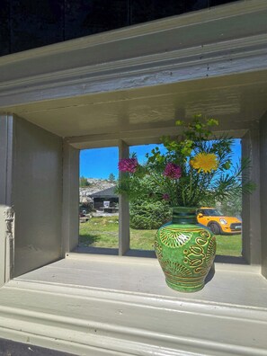 A window with a green vase containing flowers and a yellow car parked outside.