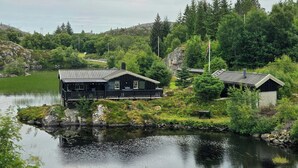 A cabin with a dock extending into a lake, surrounded by dense forest and hills.