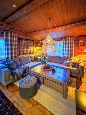 A cozy cabin interior with a wooden ceiling, a large chandelier, a sofa set, a coffee table, and a rug. - Cozy timber cabin from 1966 with sauna (Kvenvær)