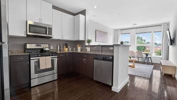 A modern kitchen with stainless steel appliances, dark wood flooring, and a view of the outdoors through large windows.