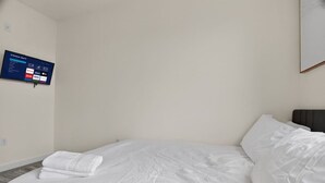 Une chambre d’hôtel avec un lit, un téléviseur à écran plat fixé au mur et un tableau encadré au-dessus du lit.