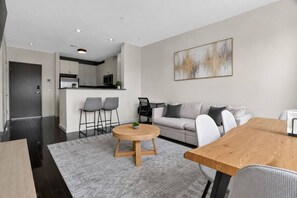 Ein modernes Wohnzimmer mit einer Couch, einem runden Holztisch und einer Küche im Hintergrund.