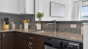 Une cuisine moderne dotée de plans de travail en granit, d’appareils électroménagers en acier inoxydable et d’armoires en bois foncé.