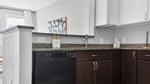Une cuisine moderne avec des meubles de couleur sombre, un lave-vaisselle et un plan de travail en granit.