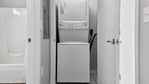 Une petite buanderie équipée d’un lave-linge et d’un sèche-linge superposés, d’une porte avec une poignée et d’un sol carrelé.