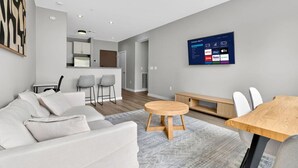 Un salon moderne avec un canapé, une table ronde en bois et un téléviseur fixé au mur, diffusant des services de streaming.