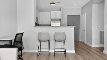 Een moderne keuken met witte kasten, een centraal eiland en twee barkrukken.