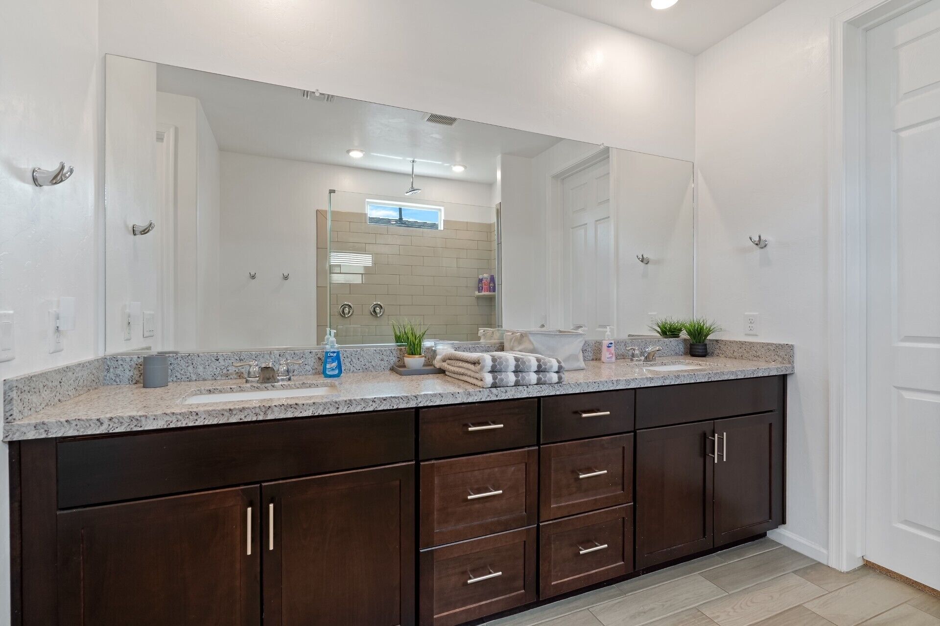 A bathroom with a large mirror, dark wooden cabinets, a granite countertop, and a shower area visible through the glass door.