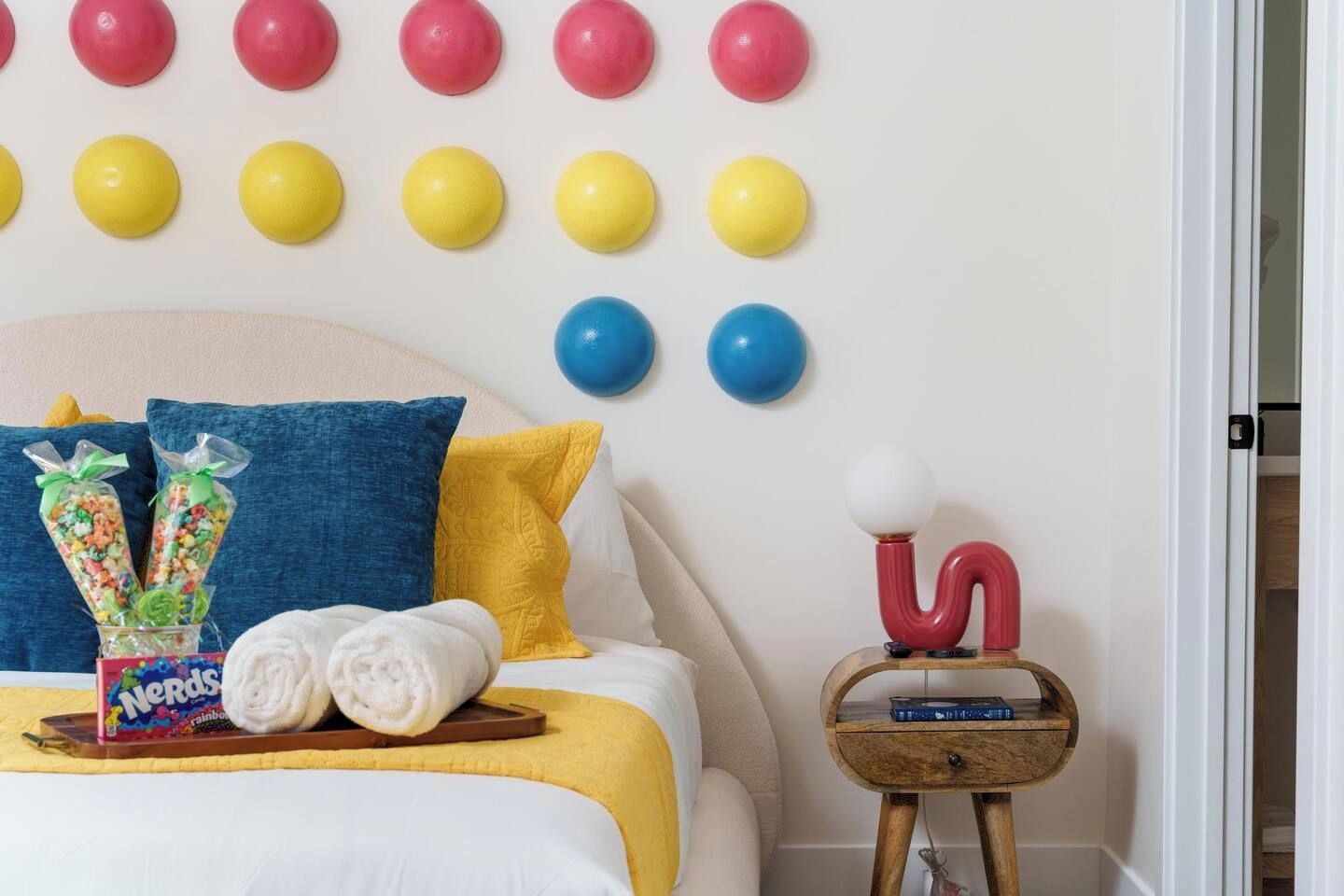 Une chambre à coucher bien rangée, avec un lit, des oreillers, une table de chevet et un mur décoré d’éléments sphériques aux couleurs vives.