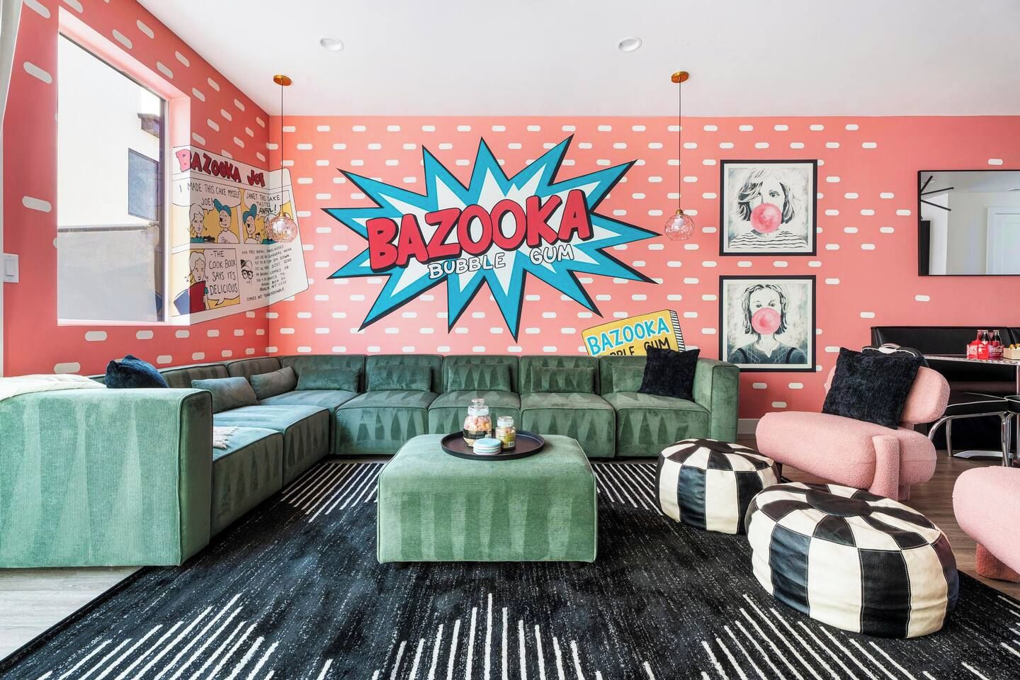 Een woonkamer met een groene bank, een zwart-wit gestreept voetenbankje en een roze fauteuil.