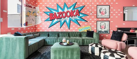 Una sala de estar con un sofá verde, un reposapiés estampado en blanco y negro, y un sillón rosa.