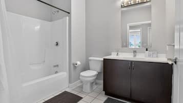 A bathroom with a walk-in shower, toilet, and dark-toned vanity with a mirror above.