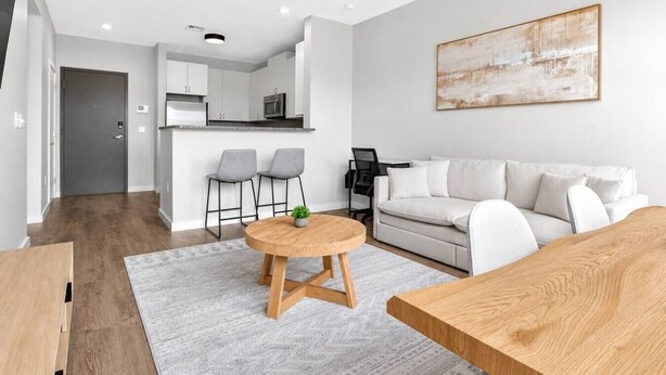 Un salon moderne avec un canapé, une table basse ronde en bois et une cuisine en arrière-plan.