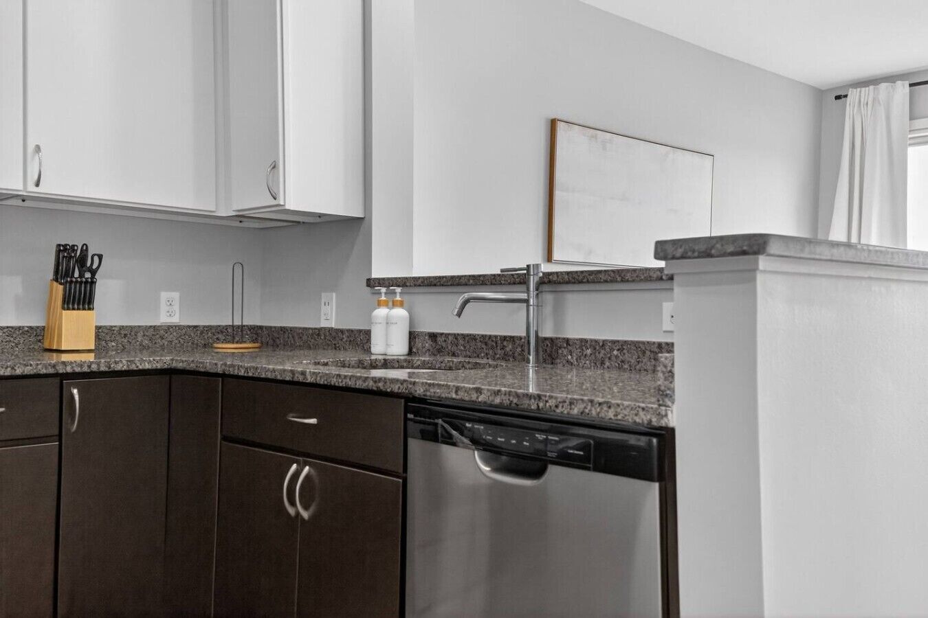 A modern kitchen with dark cabinets, a granite countertop, stainless steel dishwasher, and a white backsplash.