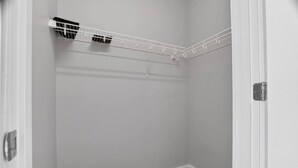 Une pièce d’angle avec une porte blanche, un radiateur blanc et une étagère blanche fixée au plafond.