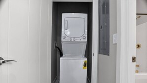 Une petite buanderie blanche, équipée d’un lave-linge et d’un sèche-linge à chargement frontal, d’une porte avec une poignée en laiton et d’un sol carrelé.