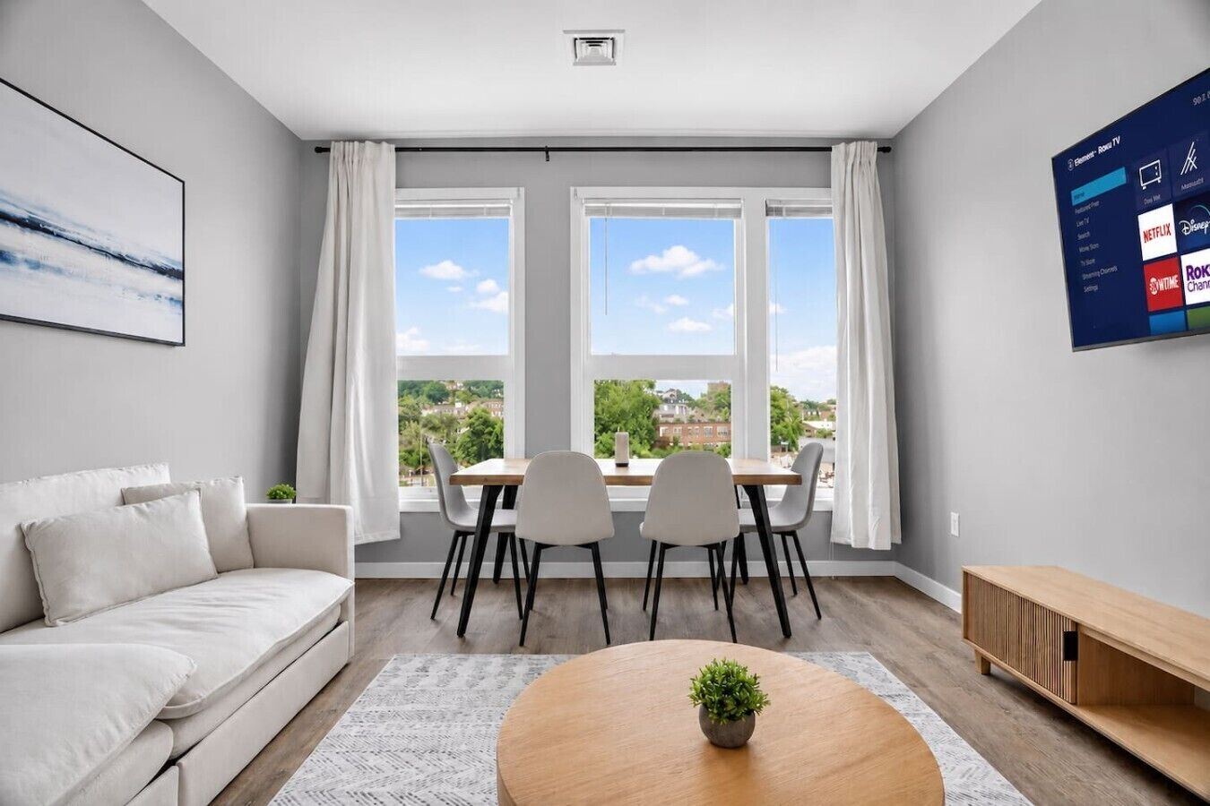 En moderne stue med sofa, spisebord, stole, sofabord og et tv der viser streamingtjenester.